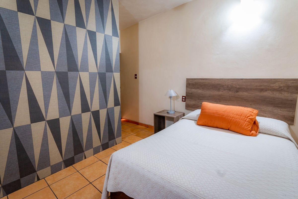 A hotel room with a bed, a nightstand, a lamp, and a geometric-patterned wall.