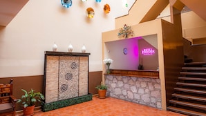 A hotel lobby with a reception desk, a staircase, and a wall decorated with colorful glass art. - Hotel Estefania (Morelia)