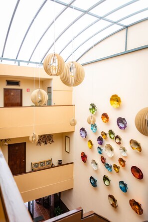 A multi-level interior with hanging spherical light fixtures and a wall adorned with colorful, abstract glass art. - Hotel Estefania (Morelia)