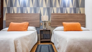 A hotel room with two beds, each with an orange pillow, a small bedside table with a lamp, and a geometric-patterned wall. - Hotel Estefania (Morelia)