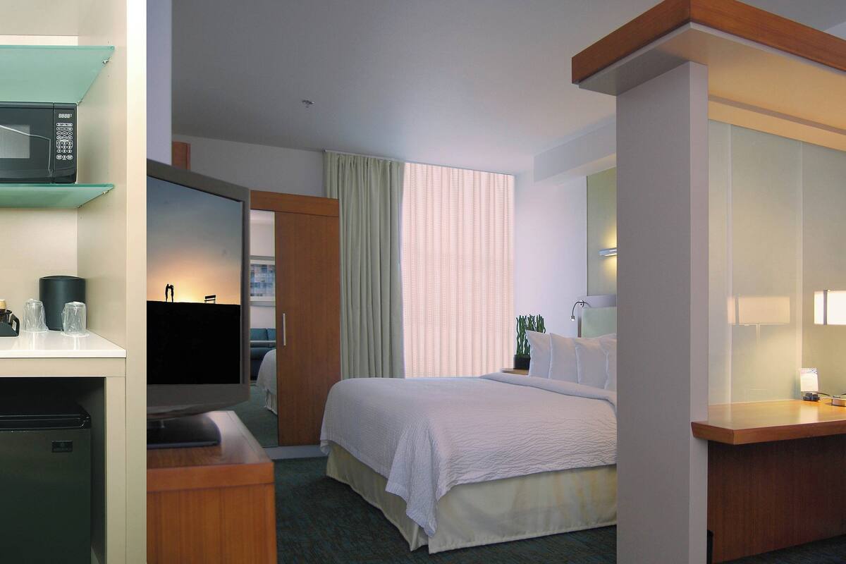 A hotel room with a bed, a television, a desk with a computer, a microwave, and a refrigerator.