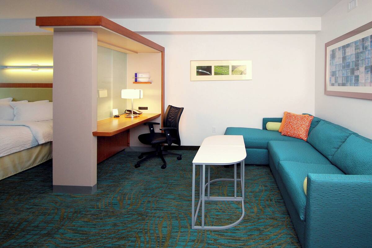 A hotel room with a bed, a desk, a chair, a sofa, and a small stool.