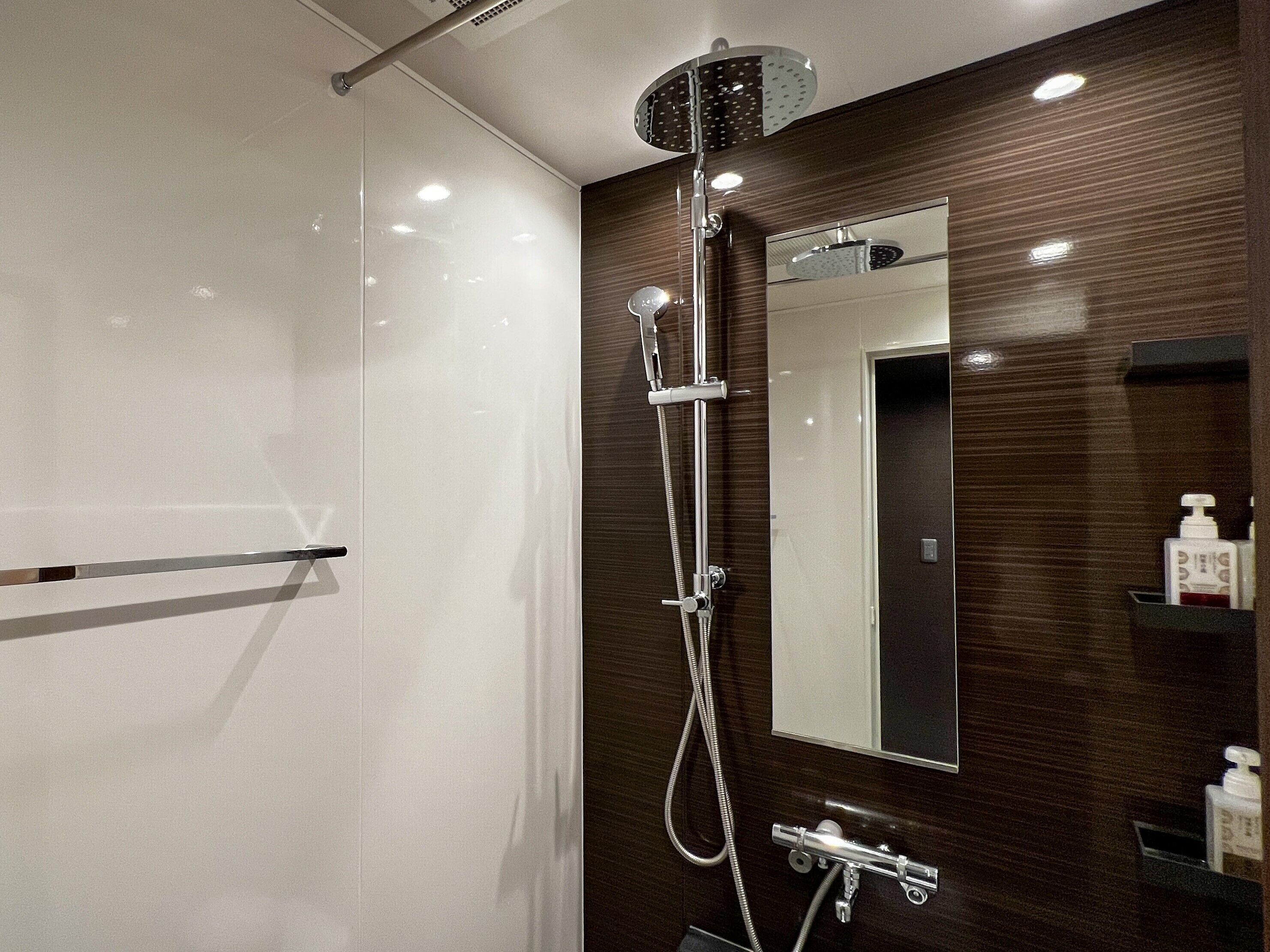 Un baño moderno con cabina de ducha de vidrio, un espejo grande y un mueble de tocador de madera con dispensador de jabón.