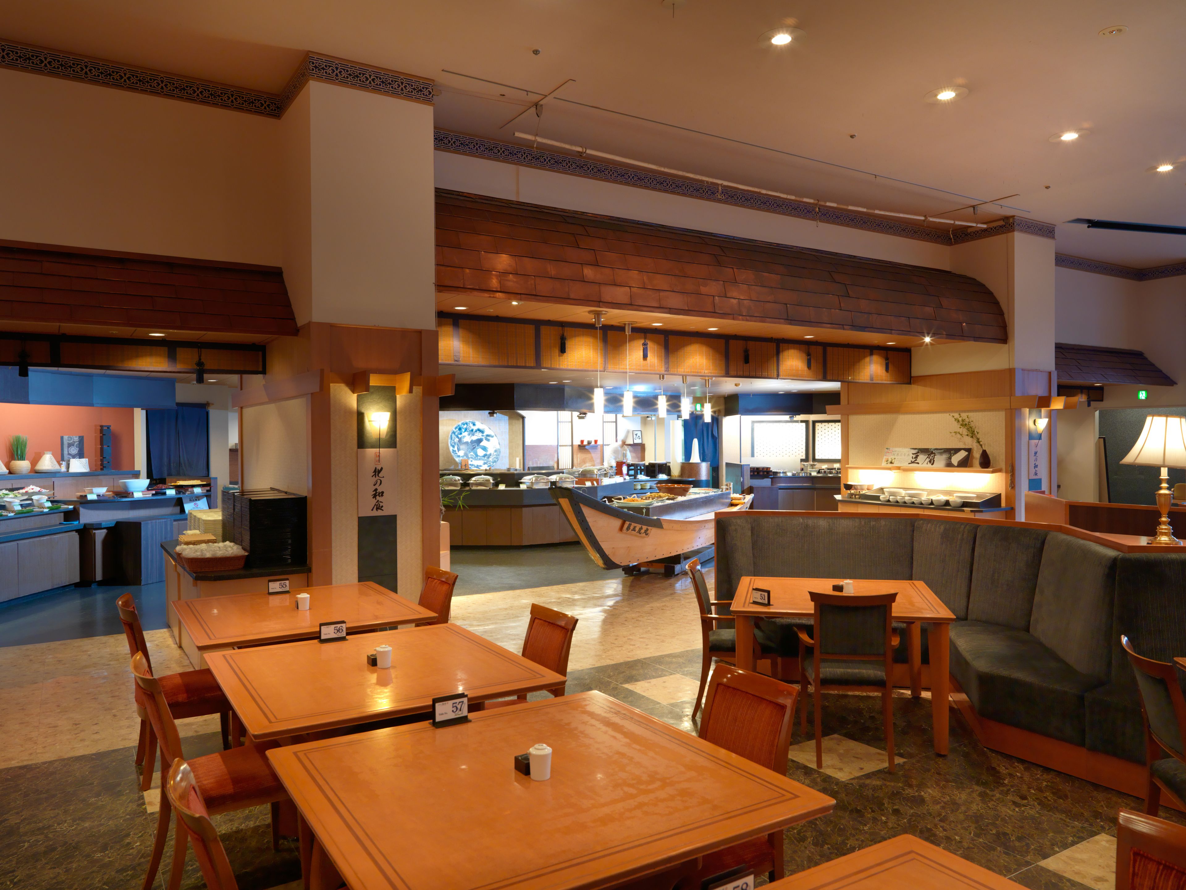 Un restaurante con varias mesas y cabinas, un área de cocina al fondo, y una pared decorativa con un diseño circular.