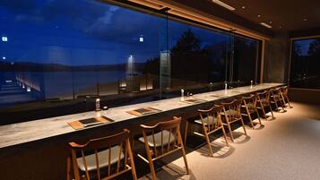A long bar with wooden chairs and a view of the outdoors at dusk.