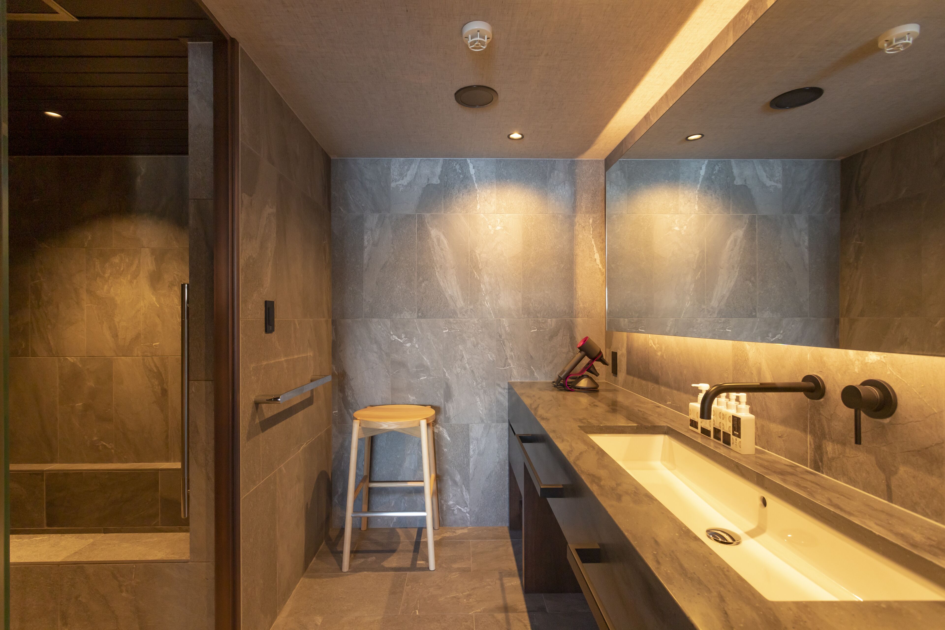 Un baño moderno con un lavamanos grande, un espejo y un taburete de madera.