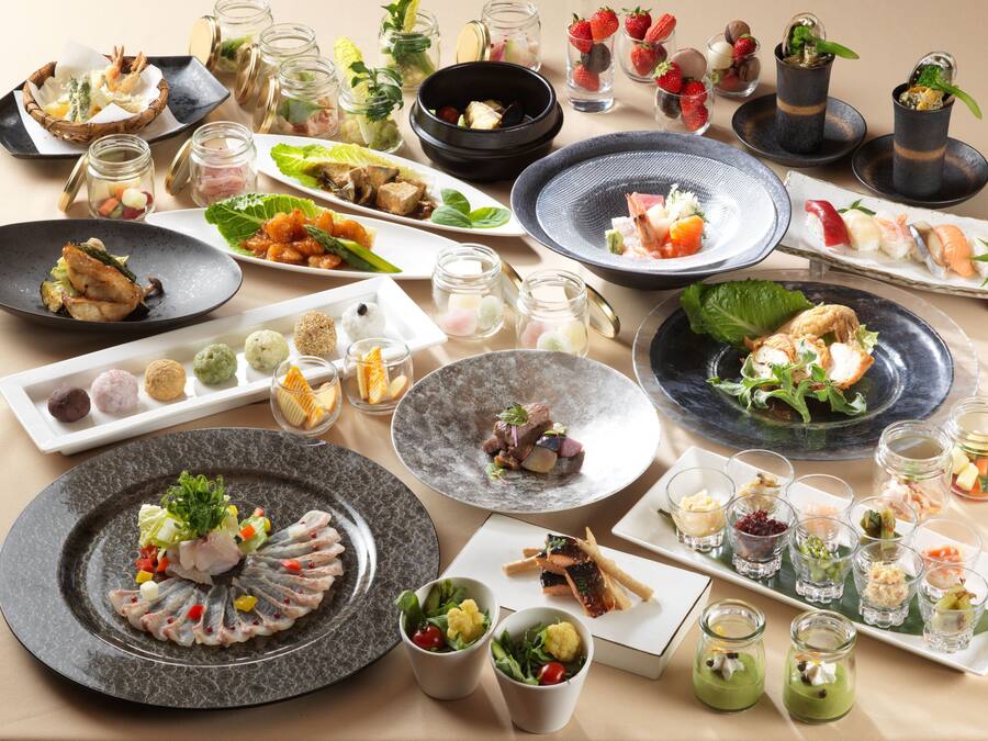 Una variedad de platillos y bebidas sobre una mesa, incluyendo sushi, sashimi y pequeños postres.