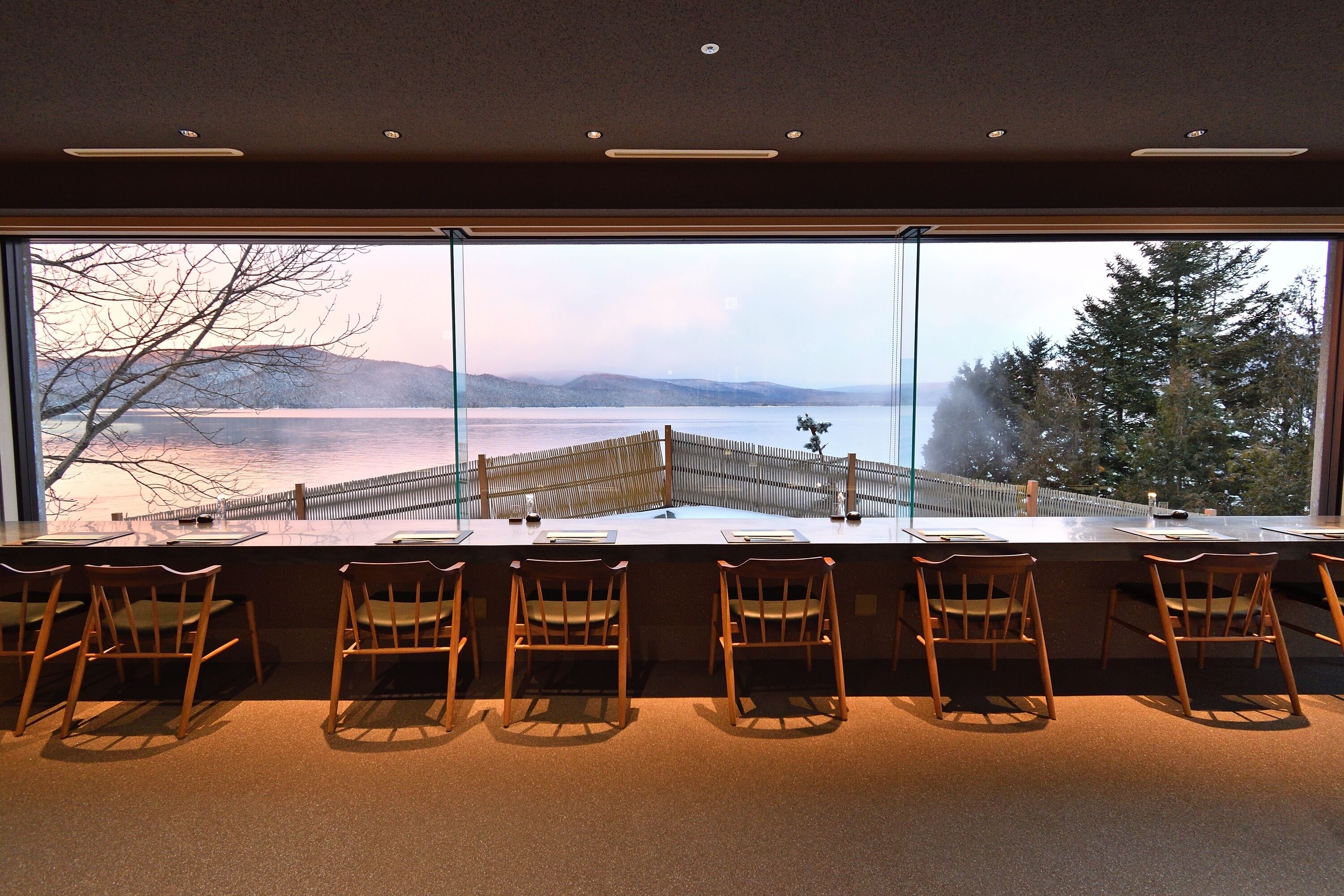 A bar area with a view of a lake and mountains through large windows.