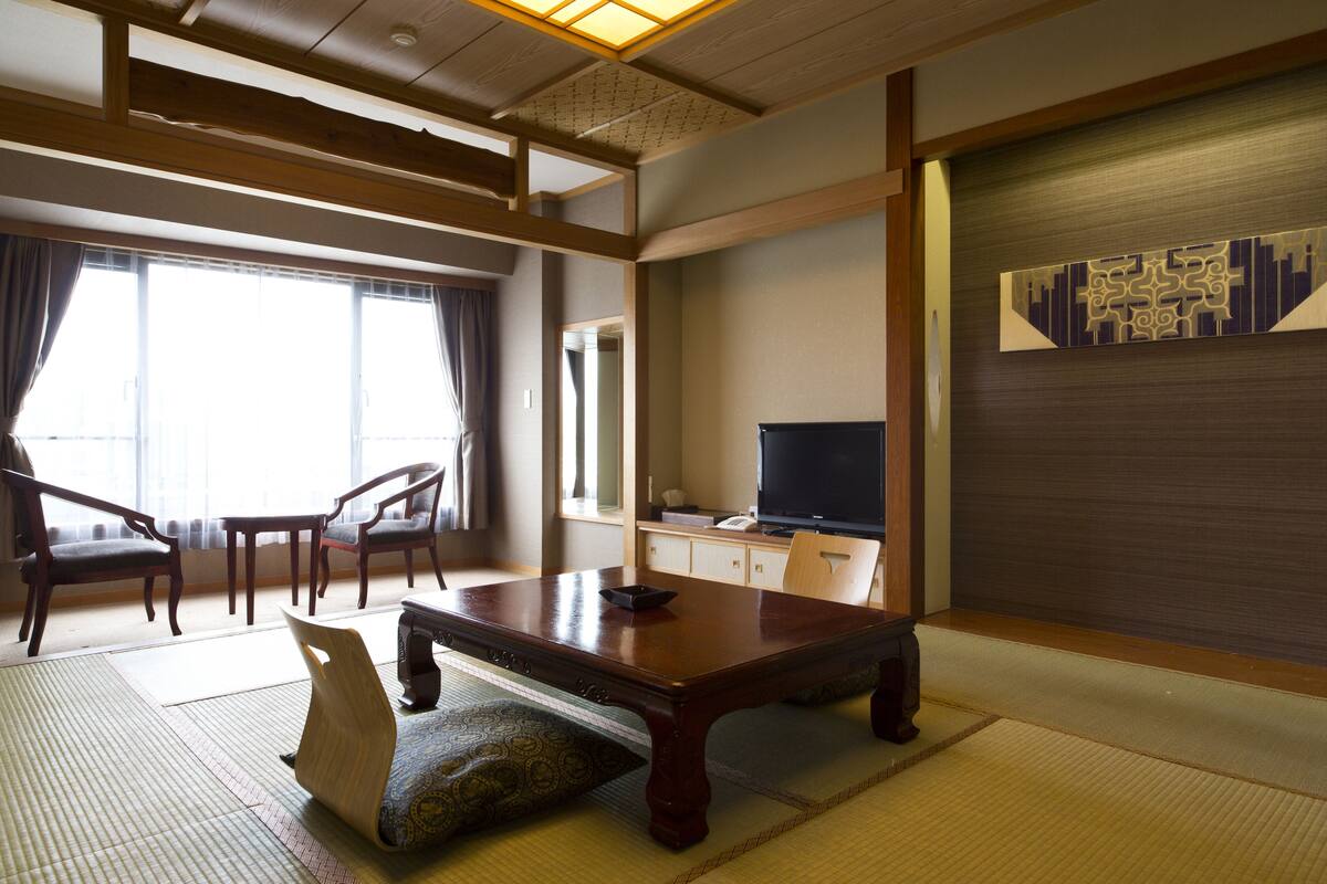 A traditional Japanese-style room with tatami flooring, a low wooden table, and a television on a cabinet.