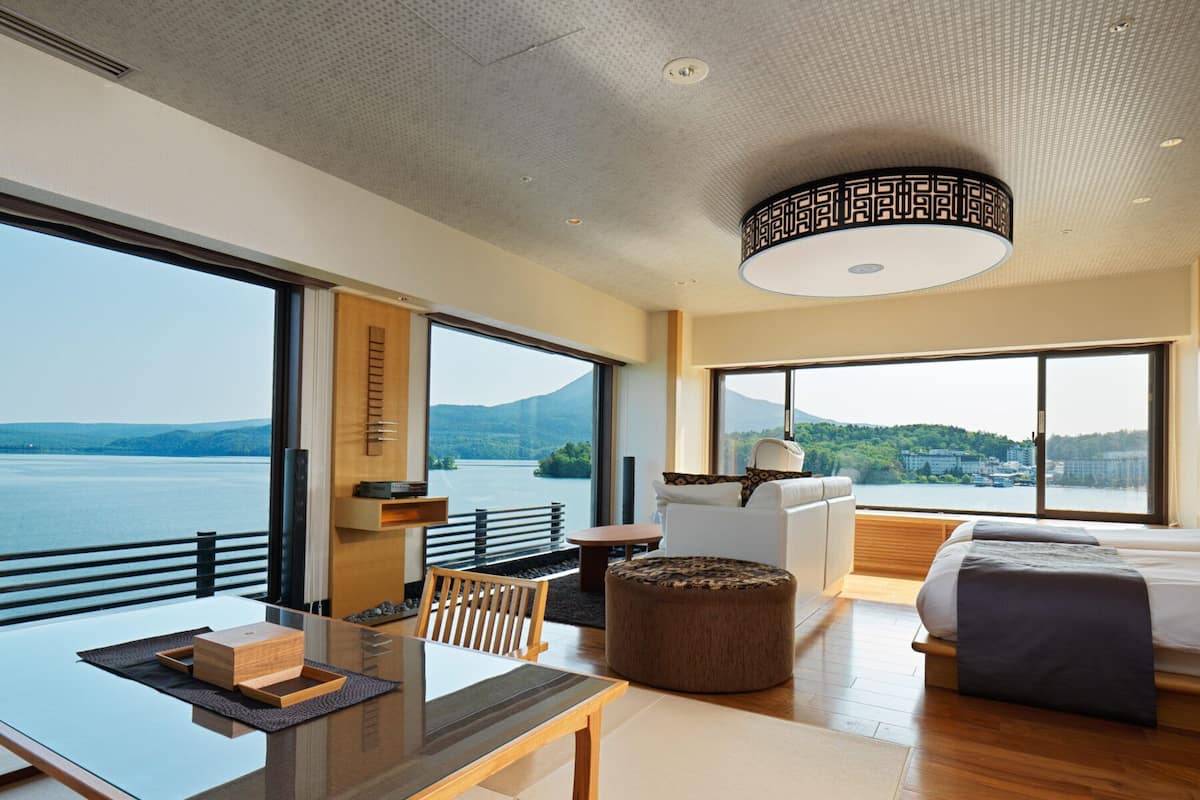A modern hotel room with a large window offering a view of a lake and mountains.