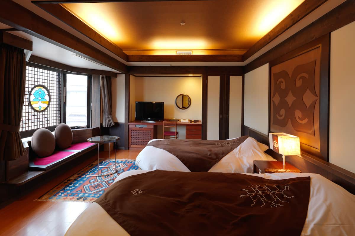 A hotel room with two beds, a TV, a desk, and a seating area with a view of the outside.