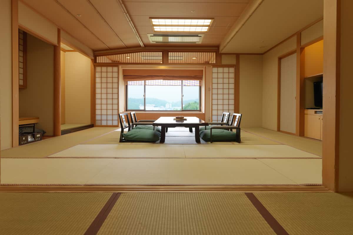 A traditional Japanese tatami room with a low table, green cushions, and sliding doors.