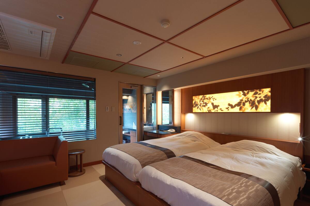 A hotel room with a large bed, a sofa, a small table, and a bathroom visible through an open door.