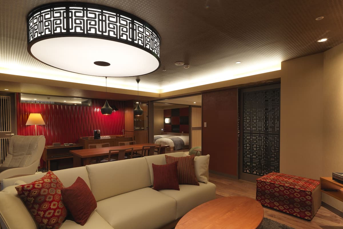 A modern living room with a sofa, a coffee table, and a dining area with a red curtain backdrop.