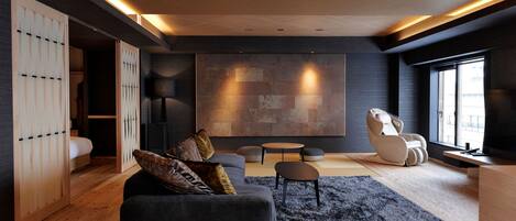 Una sala de estar moderna con un sofá oscuro, una silla blanca y una gran obra de arte abstracto en la pared.