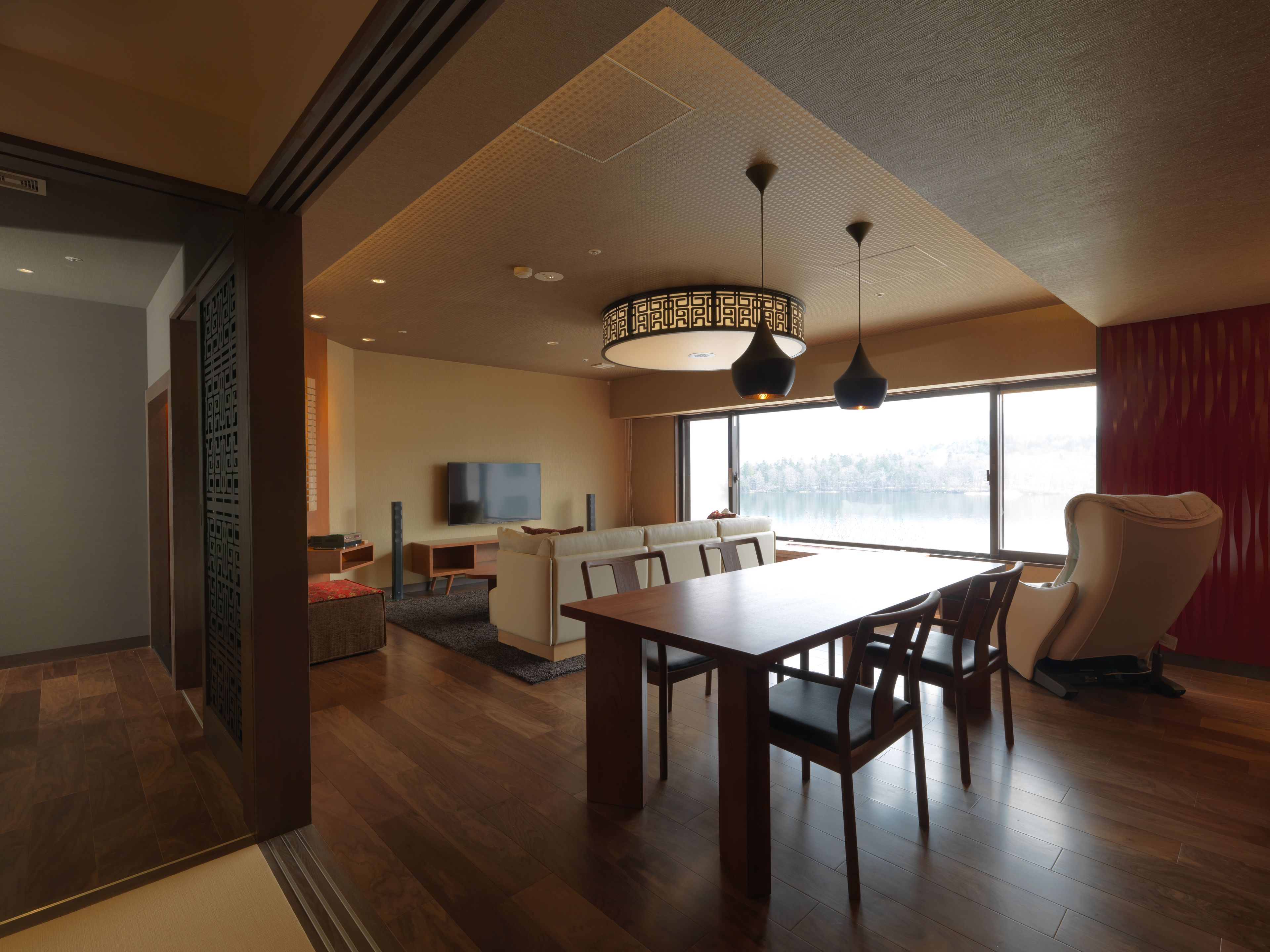 A modern living room with a wooden dining table, chairs, a sofa, and a TV.