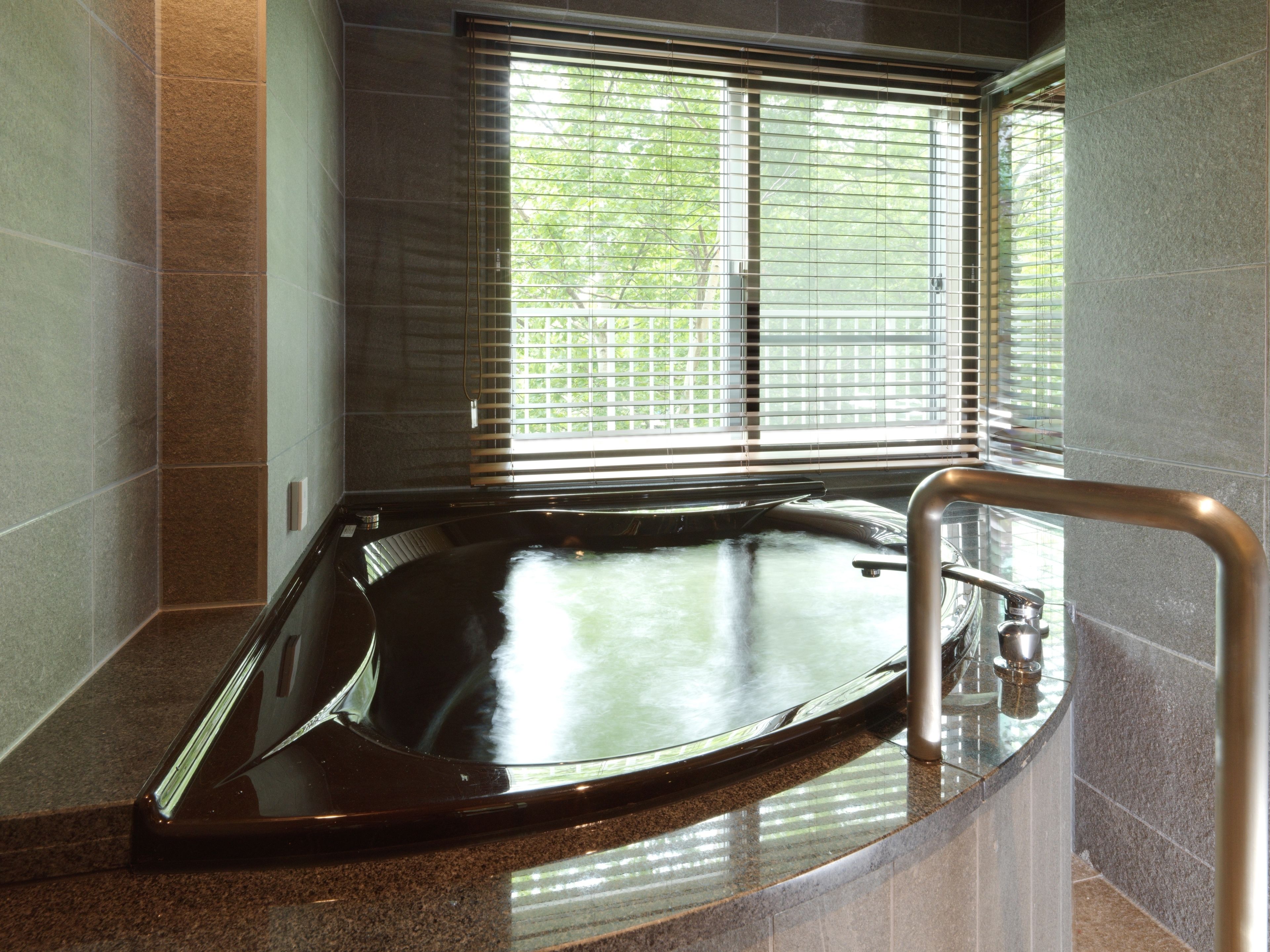 A modern bathroom with a freestanding bathtub, a glass shower enclosure, and a window with blinds.