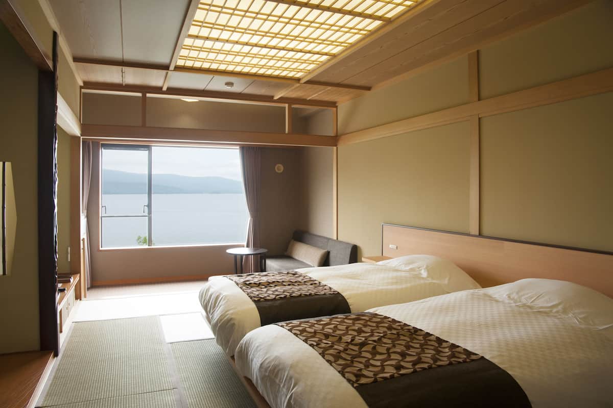 A hotel room with two beds, a view of the sea, a small table, and a traditional ceiling design.