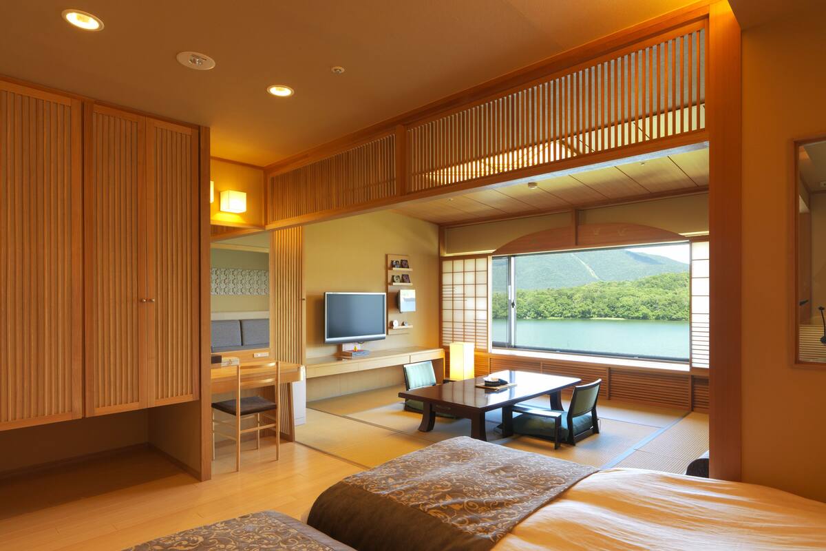 A hotel room with a large bed, a desk, a television, and a view of a lake.