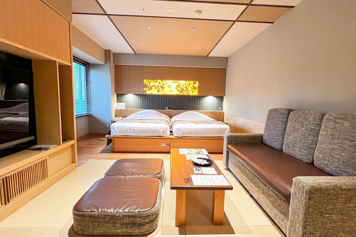 Una habitación de hotel moderna con cama, sofá, televisor y una pequeña mesa.
