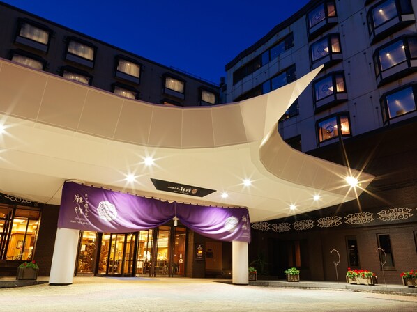 A hotel entrance with a curved overhang, a purple awning, and a sign indicating the name. - Akan Yuku no Sato Tsuruga (Kushiro)