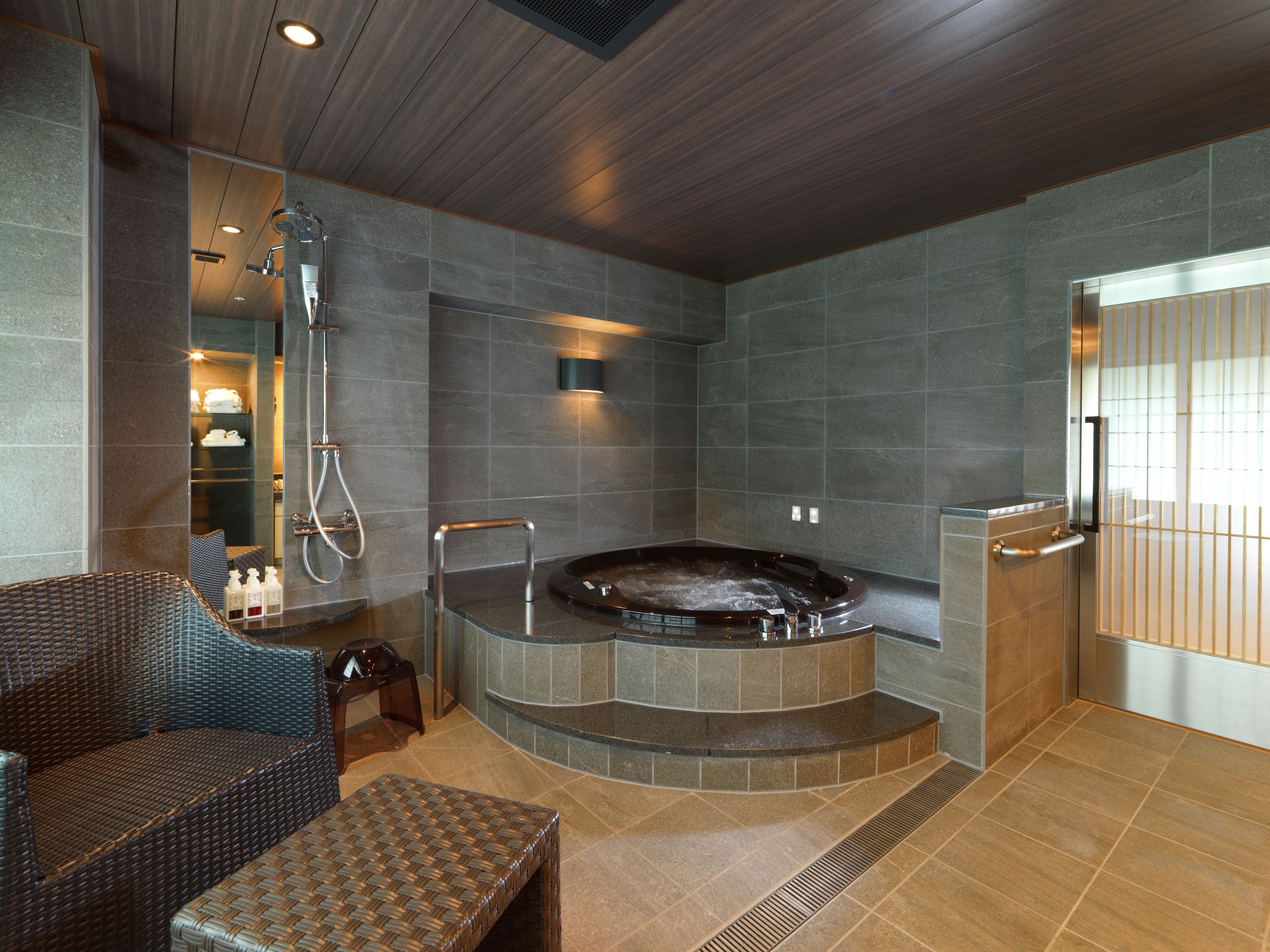 A modern bathroom with a freestanding bathtub, a glass-enclosed shower, and a seating area with wicker furniture.