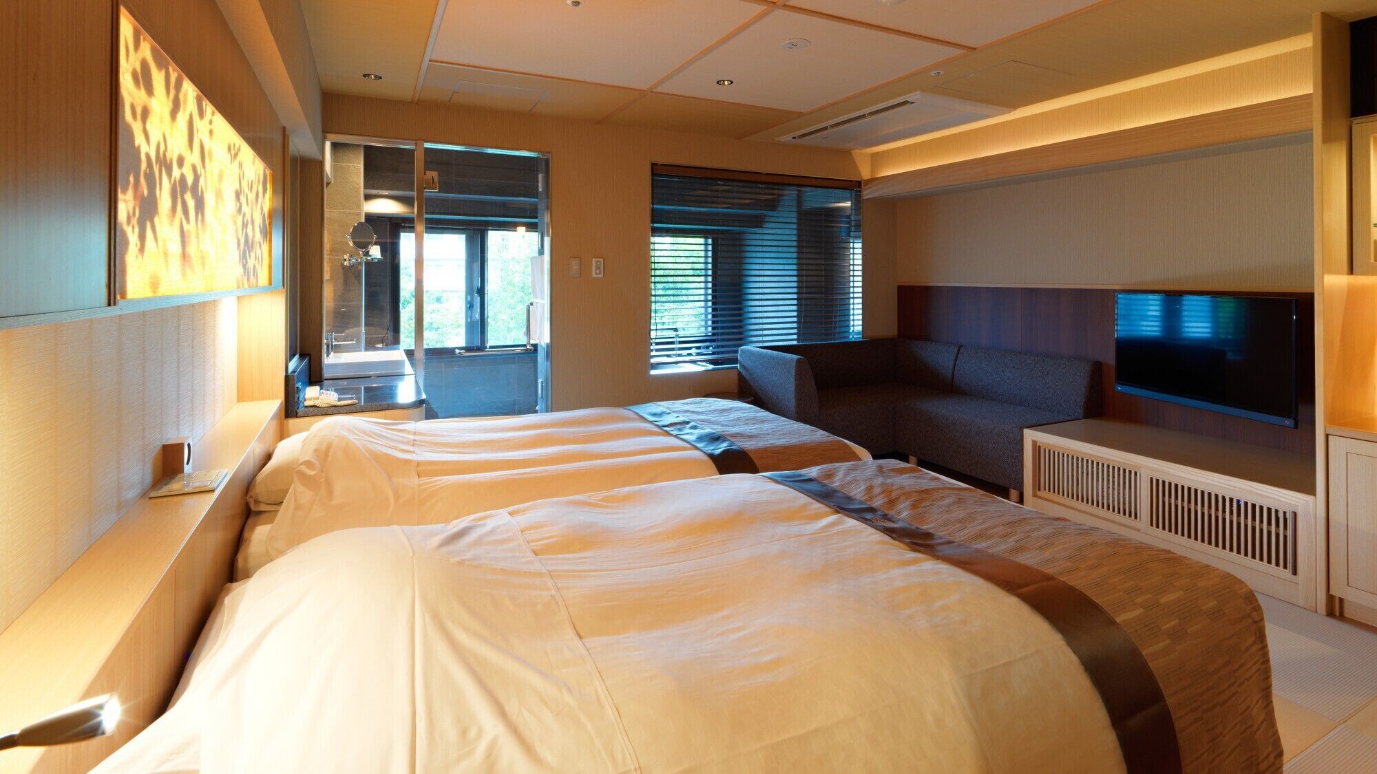 A hotel room with two beds, a sofa, a TV, and a large window.