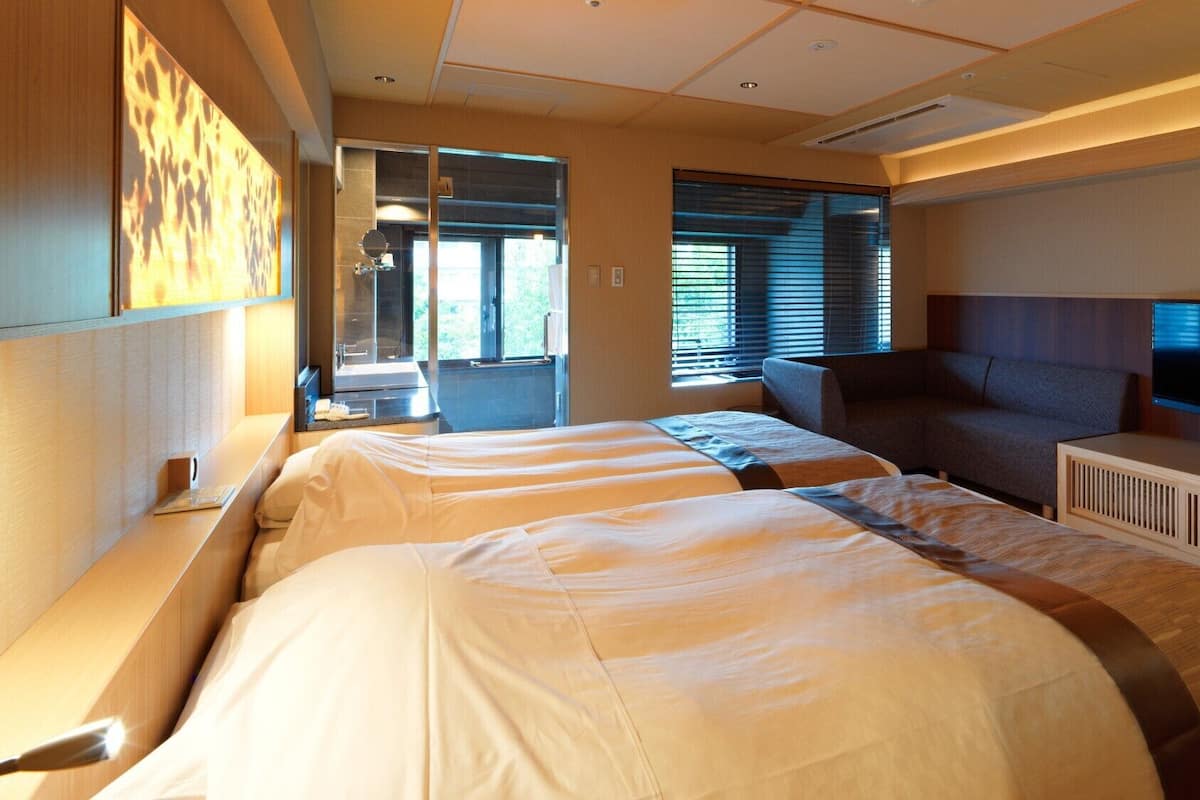 A hotel room with two beds, a sofa, a TV, and a large window.