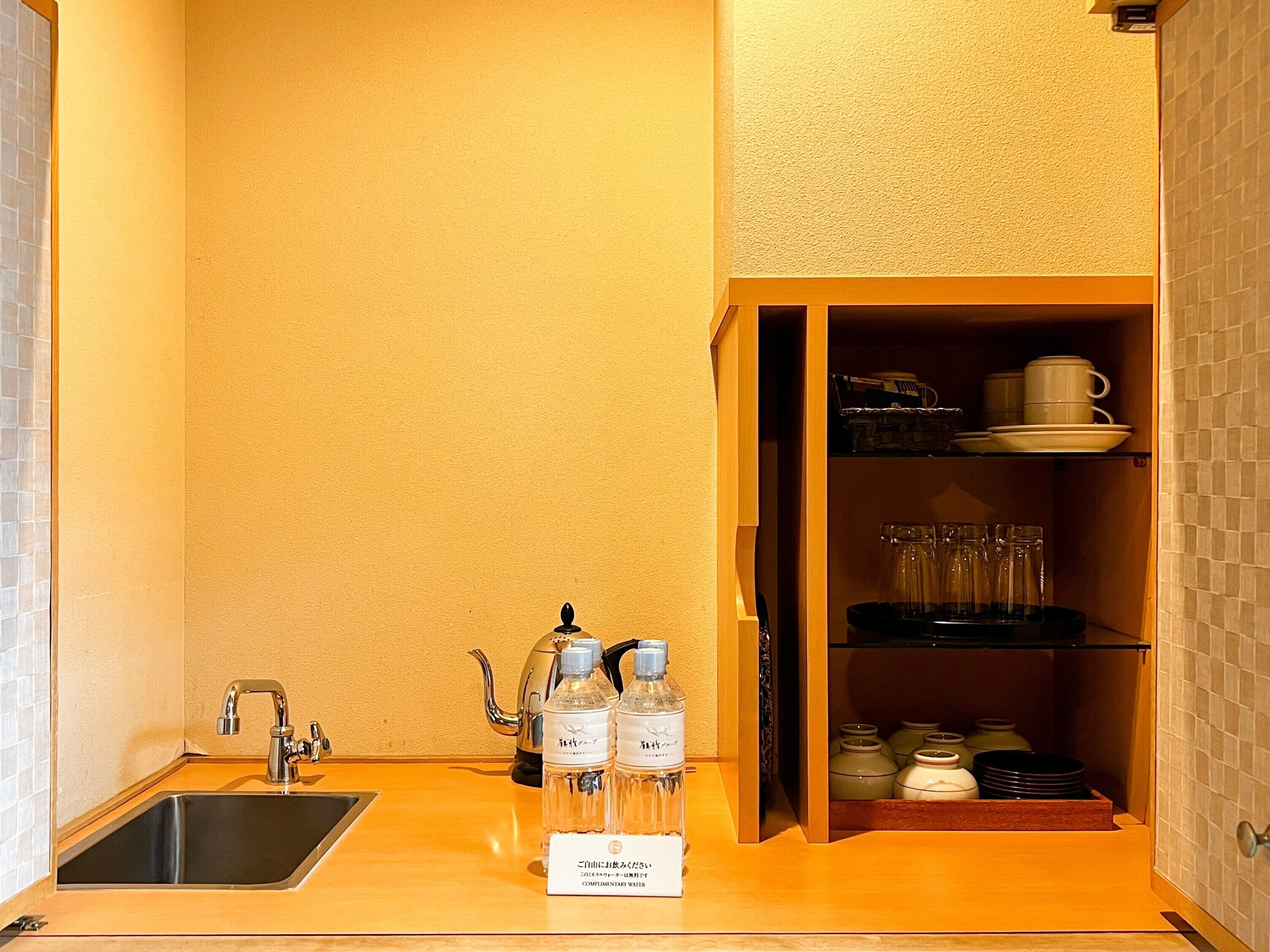 A kitchen with a sink, a kettle, and a cabinet containing dishes and glasses.