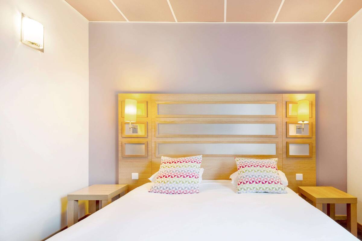 A hotel room with a large bed, two bedside tables, and a headboard with built-in lighting.
