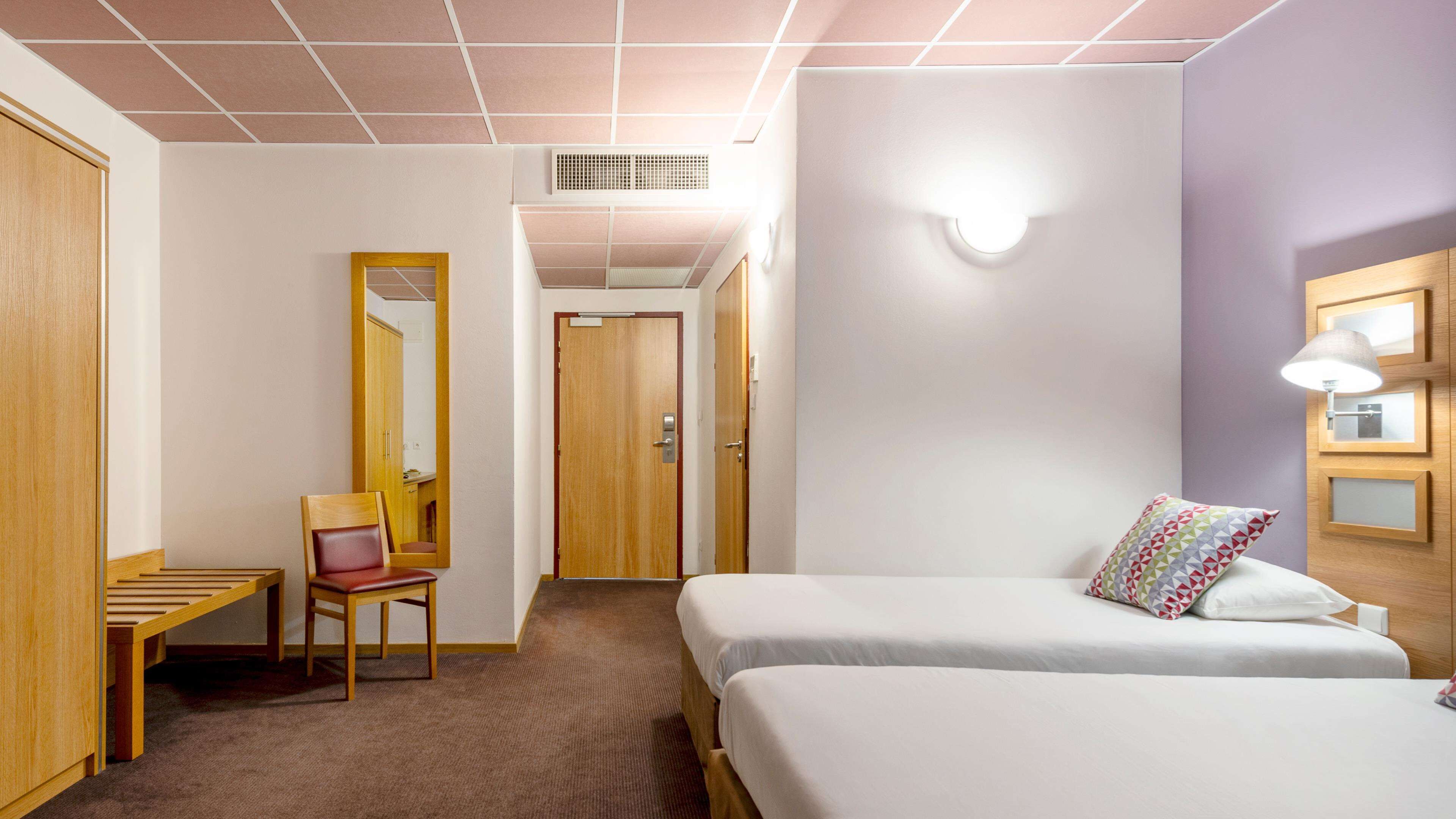 Une chambre d’hôtel avec deux lits, un bureau avec une chaise, un miroir et une lampe.
