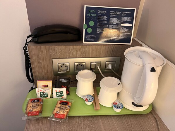 A hotel room's minibar area with a phone, a sign with French text, and various food and drink items.