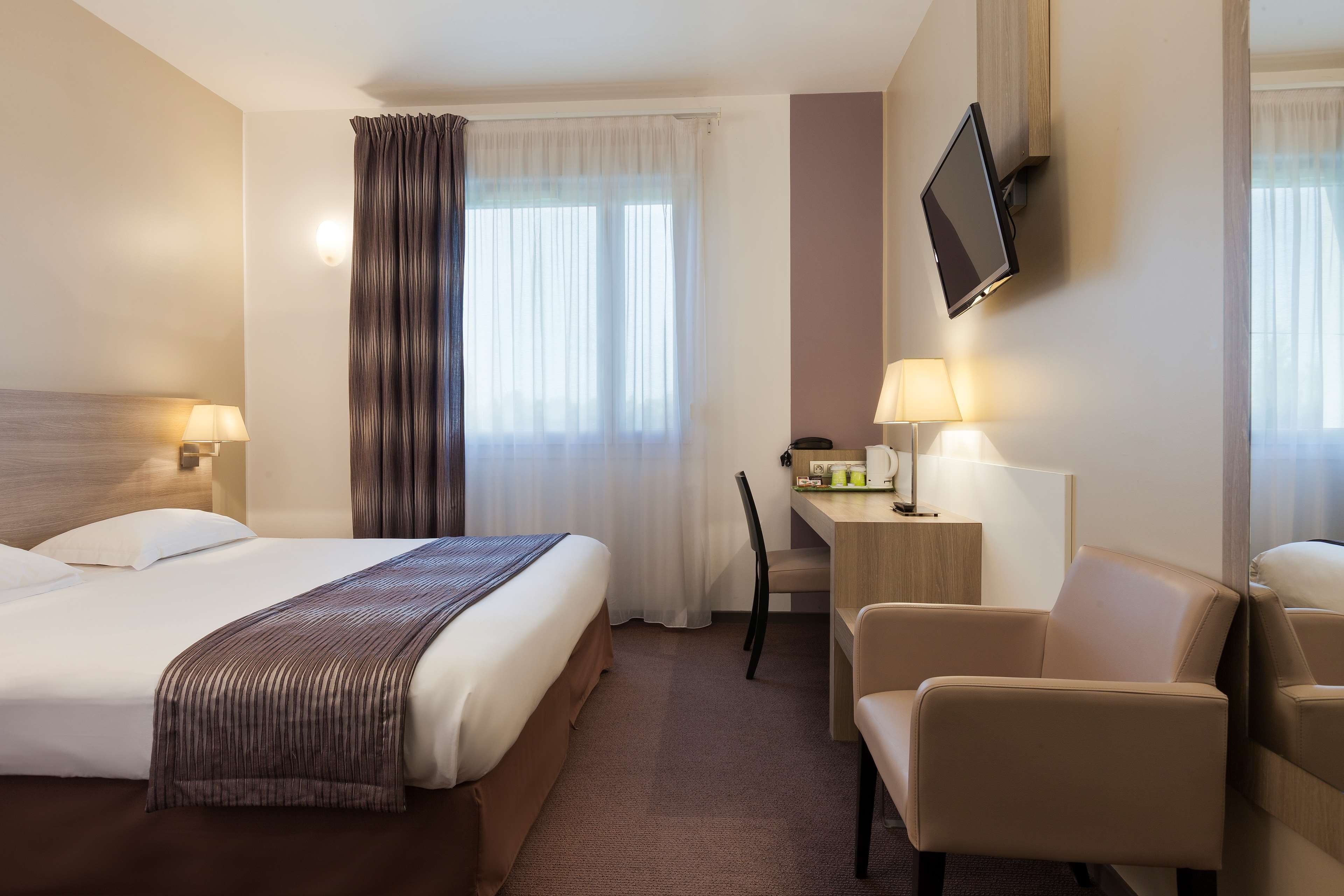 Habitación de hotel con una cama grande, un escritorio con silla, un televisor en la pared y una ventana con cortinas.