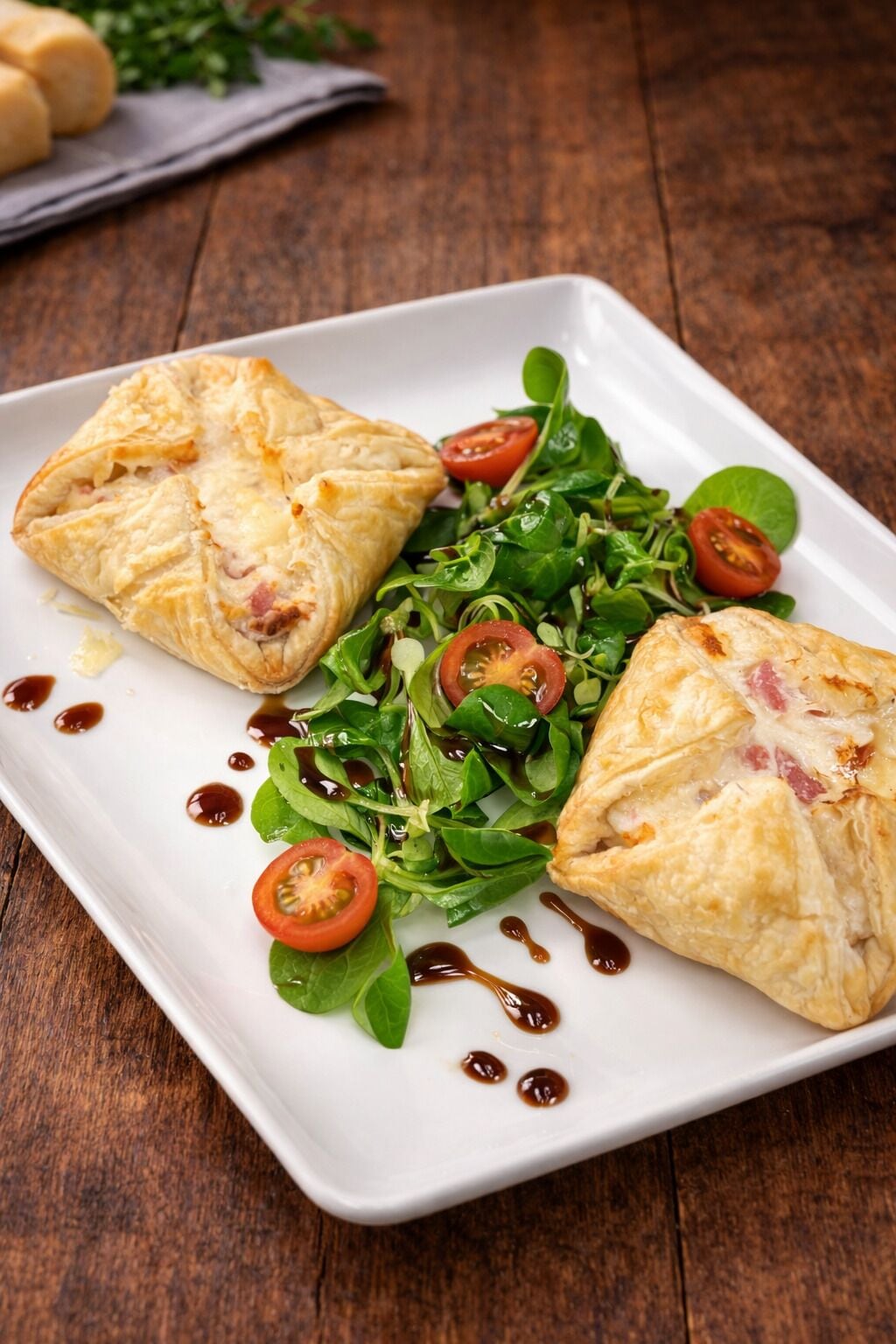 A white square plate with two golden-brown pastries and a fresh green salad with cherry tomatoes.