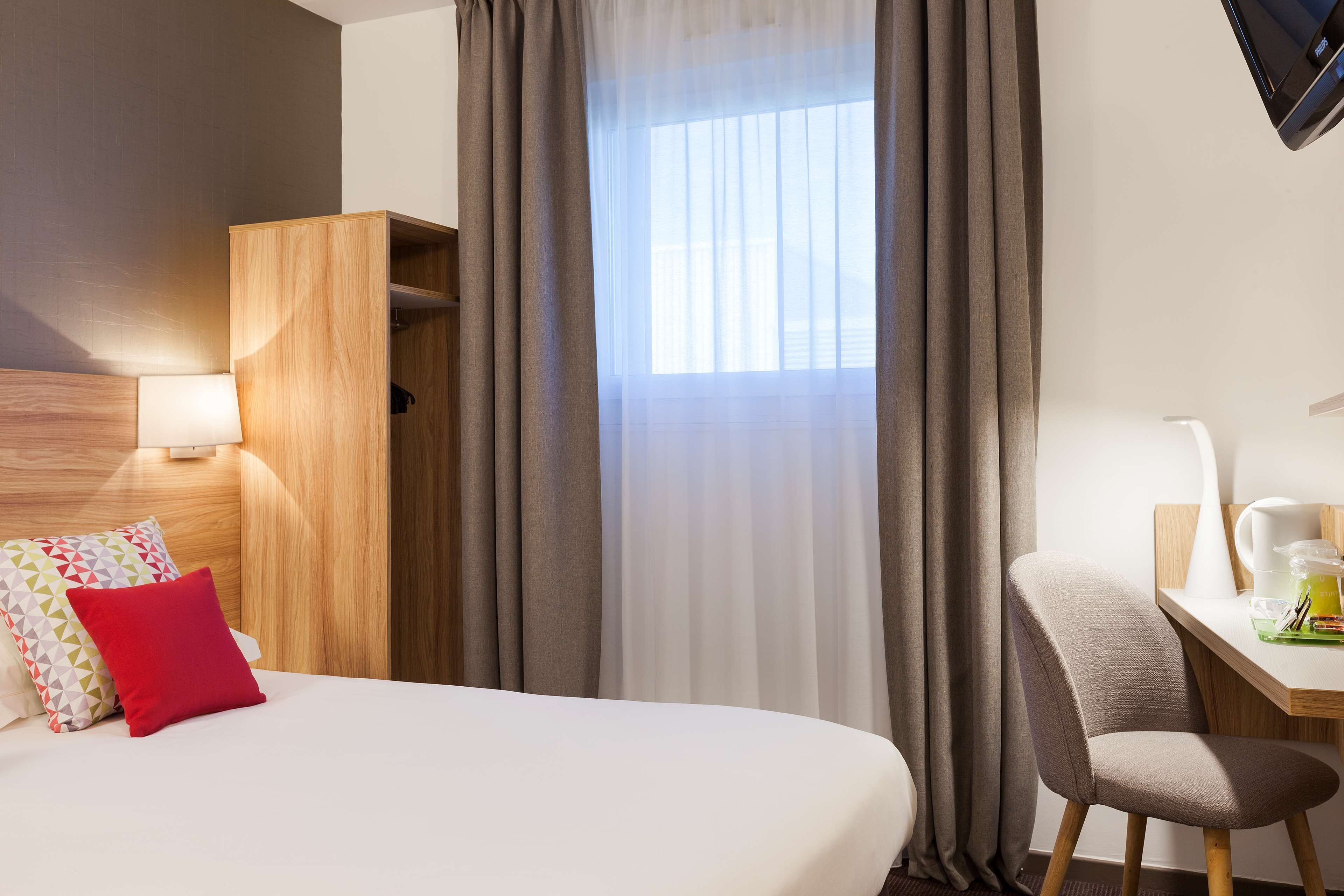 Ein Hotelzimmer mit Bett, Schreibtisch, Stuhl, Kleiderschrank und einem Fenster mit Vorhängen.