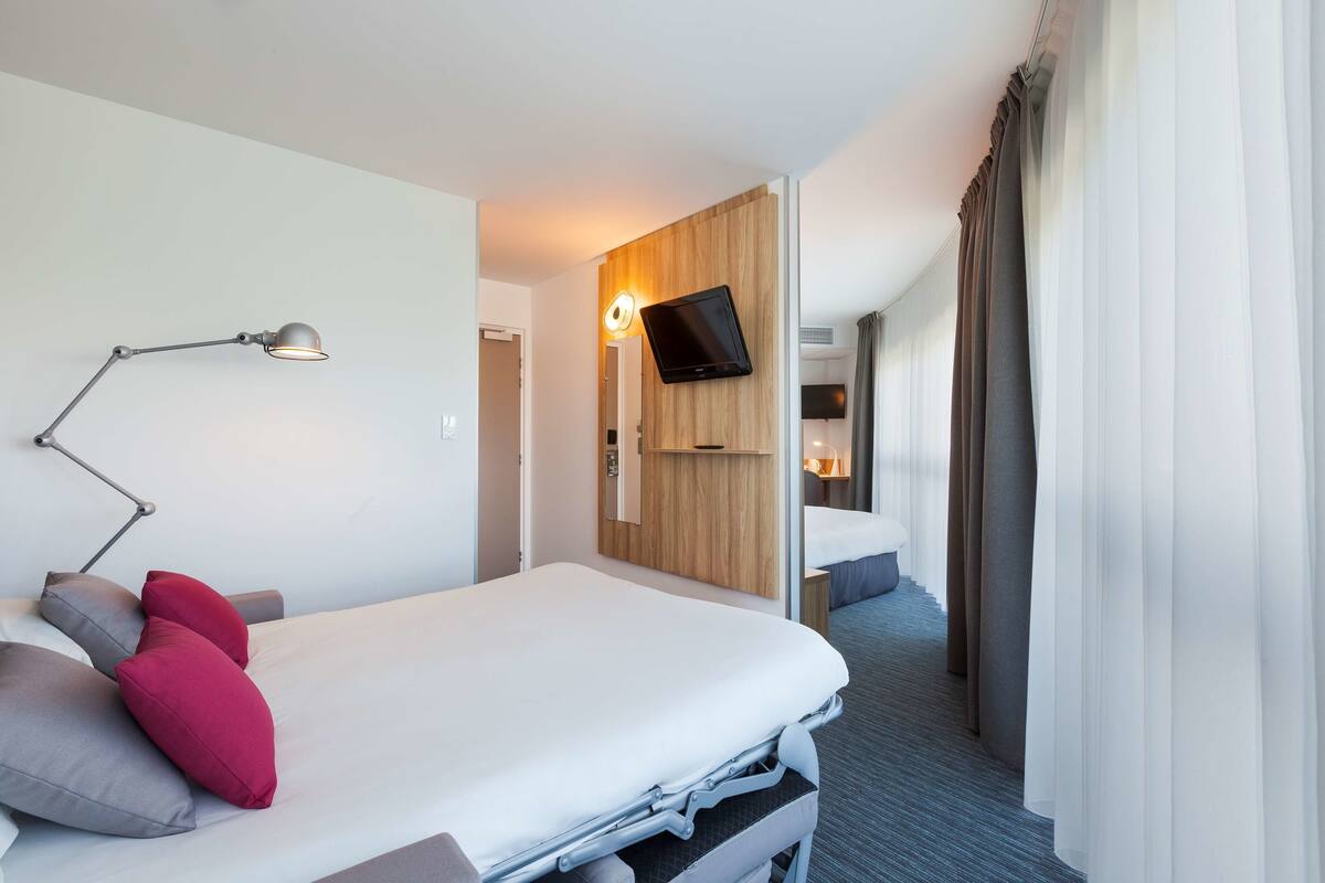A modern hotel room with a bed, a desk, a lamp, and a TV.