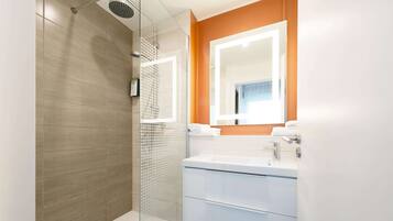 Un baño moderno con ducha envuelta en vidrio, un lavabo blanco con espejo y suelo de madera.