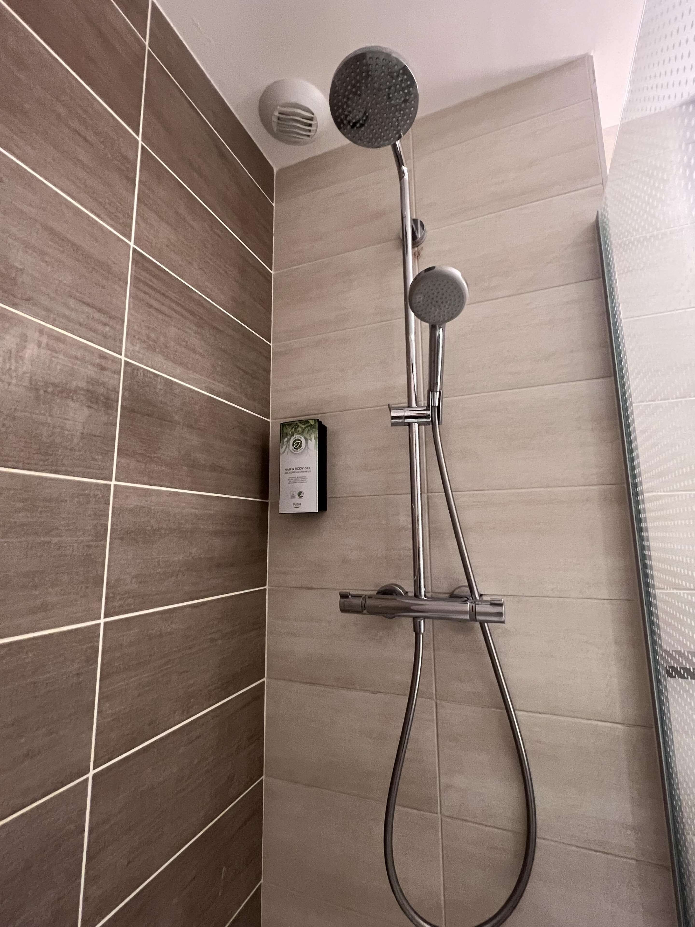 Una ducha moderna con cabezal de ducha de mano y cabezal de ducha fijo montado en la pared, con un diseño de baldosas en cuadrícula.