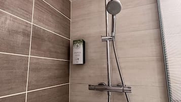 A modern shower with a handheld showerhead and a fixed wall-mounted showerhead, mounted on a wall with a grid pattern of tiles.