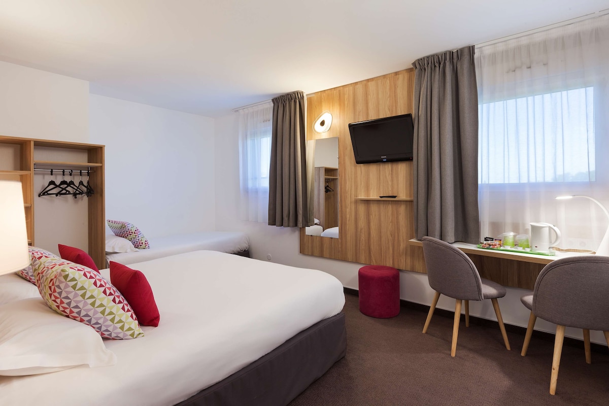Hotellihuone, jossa on sänky, työpöytä, tuoli, televisio ja naulakko.