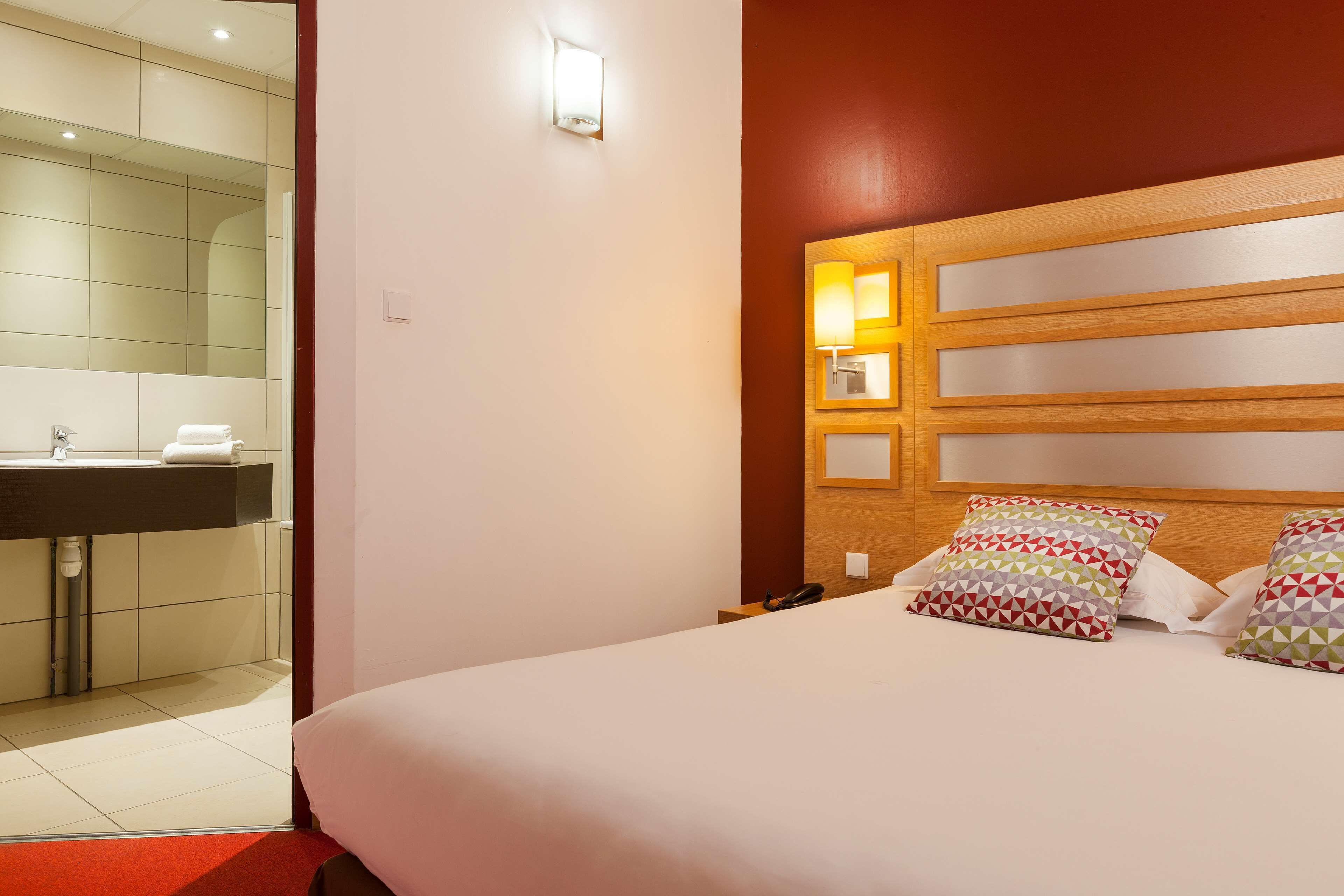 A hotel room with a bed, bedside table, and a nightstand with a phone.