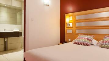 A hotel room with a bed, bedside table, and a nightstand with a phone.