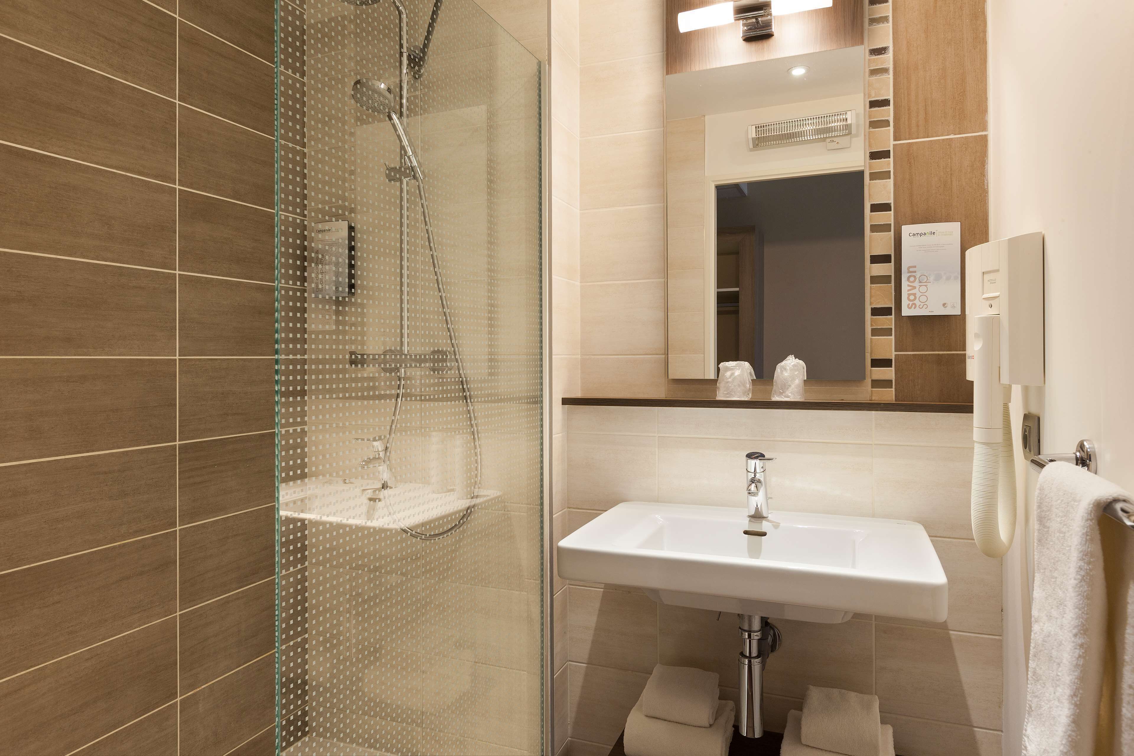 Un baño moderno con ducha envuelta en vidrio, lavamanos blanco y espejo sobre él.
