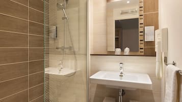 Ein modernes Badezimmer mit einer gläsernen Duschkabine, einem weißen Waschbecken und einem Spiegel darüber.