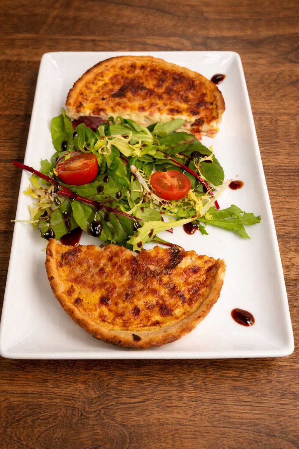 A white rectangular plate with a grilled sandwich and a salad on a wooden table.