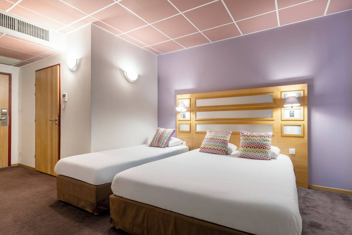 A hotel room with two beds, a wooden headboard, wall-mounted lights, and a door.