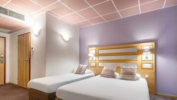 Habitación de hotel con dos camas, cabecero de madera, luces fijadas a la pared y una puerta.