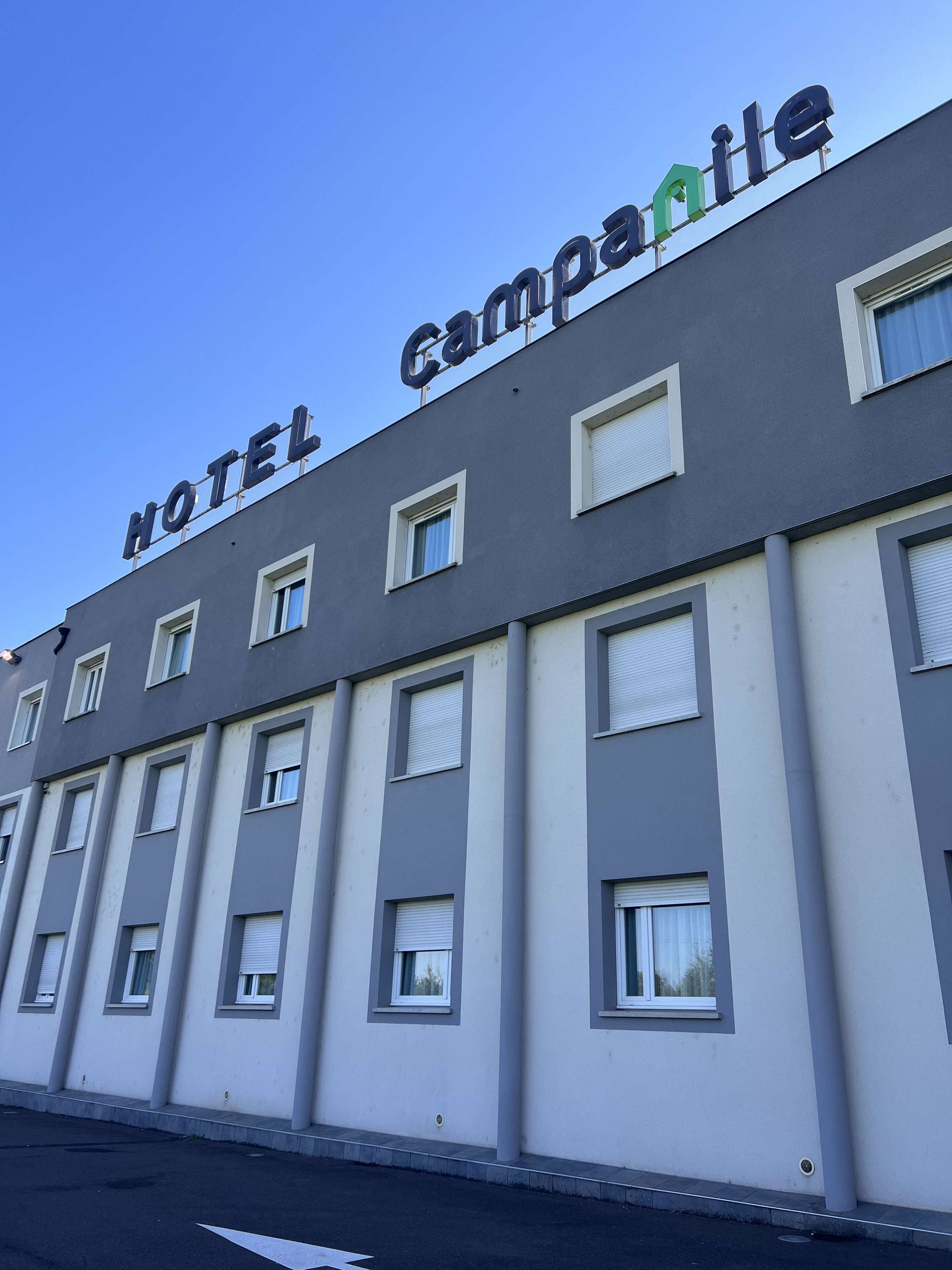 A hotel building with a sign reading "HOTEL CAMPANILE" and multiple windows with shutters.