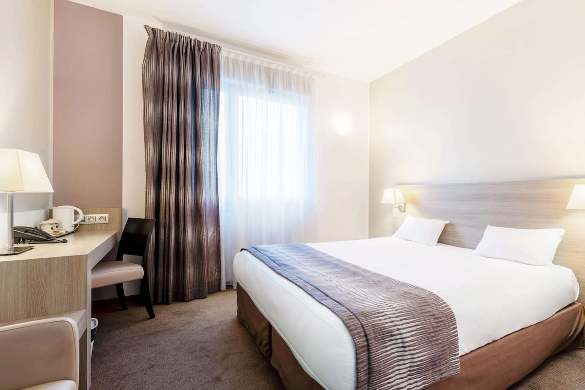 A hotel room with a bed, bedside lamps, a desk with a telephone, and a chair.