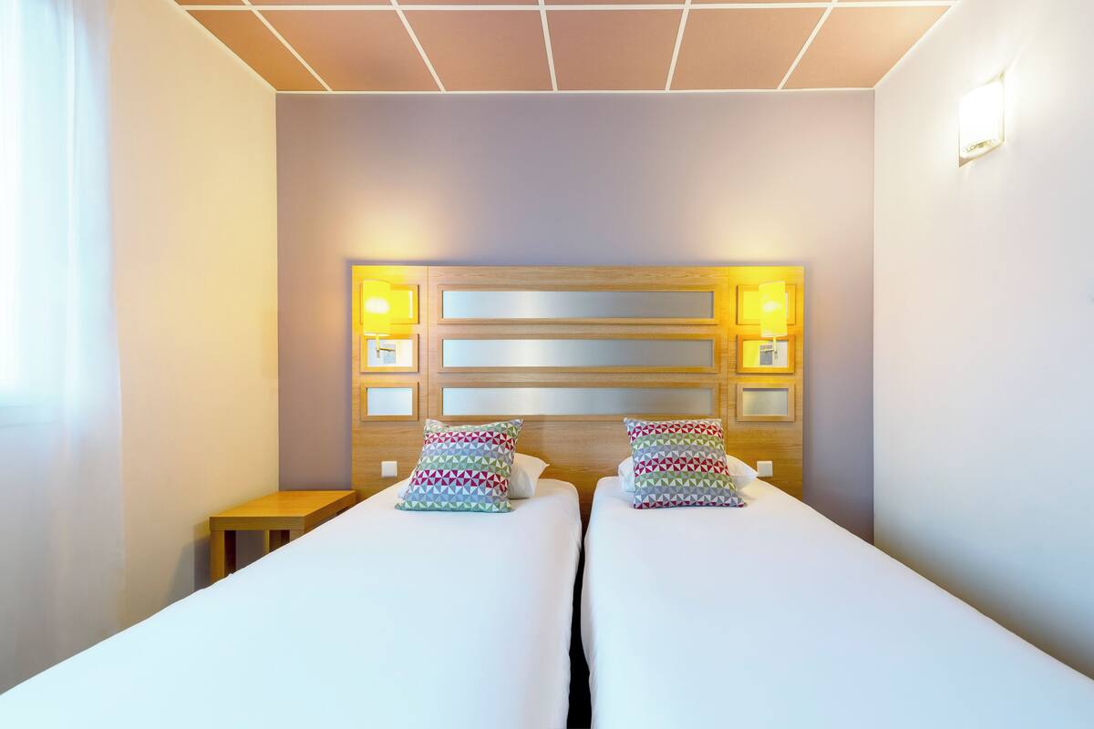 A hotel room with two beds, a wooden headboard, bedside lamps, and a small wooden table.